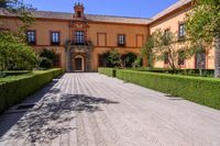 a cobblestone walkway lined with shrubbery and hedges and doors on a yellow building