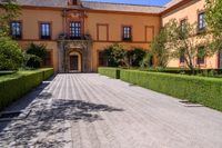 a cobblestone walkway lined with shrubbery and hedges and doors on a yellow building