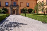 a cobblestone walkway lined with shrubbery and hedges and doors on a yellow building