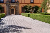 a cobblestone walkway lined with shrubbery and hedges and doors on a yellow building