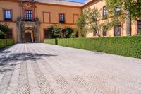 a cobblestone walkway lined with shrubbery and hedges and doors on a yellow building