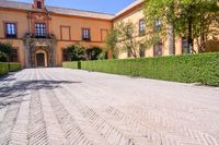 a cobblestone walkway lined with shrubbery and hedges and doors on a yellow building