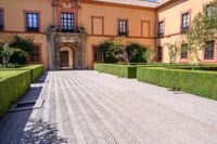 a cobblestone walkway lined with shrubbery and hedges and doors on a yellow building