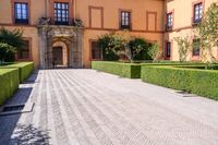 a cobblestone walkway lined with shrubbery and hedges and doors on a yellow building