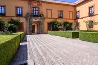 a cobblestone walkway lined with shrubbery and hedges and doors on a yellow building