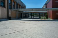 a building with windows and wood walls and doors at the bottom of it, in front of a sidewalk and concrete walkway