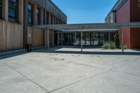 a building with windows and wood walls and doors at the bottom of it, in front of a sidewalk and concrete walkway