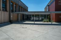 a building with windows and wood walls and doors at the bottom of it, in front of a sidewalk and concrete walkway