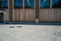 a parking meter on concrete outside a building with glass windows next to it and a wooden bench