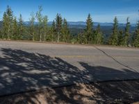 the mountains are visible in the distance from this wide, empty road, overlooking a wide landscape and forest