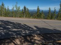 the mountains are visible in the distance from this wide, empty road, overlooking a wide landscape and forest