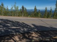 the mountains are visible in the distance from this wide, empty road, overlooking a wide landscape and forest