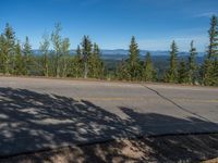 the mountains are visible in the distance from this wide, empty road, overlooking a wide landscape and forest