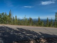 the mountains are visible in the distance from this wide, empty road, overlooking a wide landscape and forest