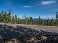 the mountains are visible in the distance from this wide, empty road, overlooking a wide landscape and forest