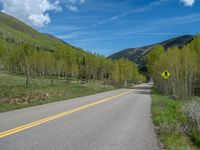 a yellow and black sign is on the street near some mountains and trees in the distance