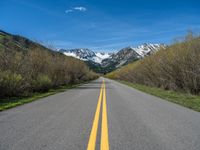 the road is paved with yellow markings and has a snowy mountain range in the background