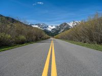 the road is paved with yellow markings and has a snowy mountain range in the background