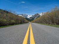 the road is paved with yellow markings and has a snowy mountain range in the background