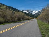 the road is paved with yellow markings and has a snowy mountain range in the background