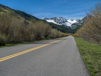 the road is paved with yellow markings and has a snowy mountain range in the background