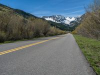 the road is paved with yellow markings and has a snowy mountain range in the background