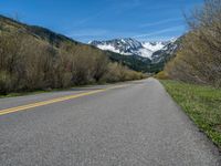 the road is paved with yellow markings and has a snowy mountain range in the background