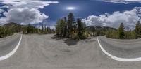 two roads are shown in this fish eye view to the sky with clouds above the road and mountain range