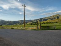 a lone country road is in the countryside area with mountains on both sides and barbed fence between the two sides