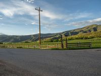 a lone country road is in the countryside area with mountains on both sides and barbed fence between the two sides