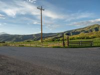 a lone country road is in the countryside area with mountains on both sides and barbed fence between the two sides