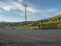 a lone country road is in the countryside area with mountains on both sides and barbed fence between the two sides