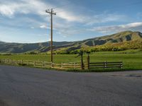 a lone country road is in the countryside area with mountains on both sides and barbed fence between the two sides