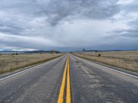 a long street passes a prairie area and mountains in the distance with heavy clouds in the sky