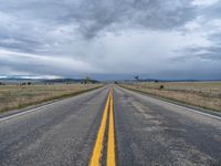 a long street passes a prairie area and mountains in the distance with heavy clouds in the sky