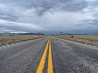 a long street passes a prairie area and mountains in the distance with heavy clouds in the sky