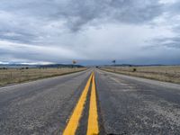 a long street passes a prairie area and mountains in the distance with heavy clouds in the sky