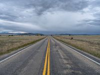 a long street passes a prairie area and mountains in the distance with heavy clouds in the sky