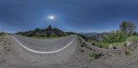 three fisheye image with a bend road between two mountains in the distance, with a man riding a skateboard below