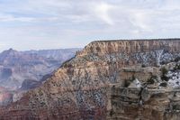 a large cliff surrounded by canyon covered in snow and rock formations is near the edge of a canyon