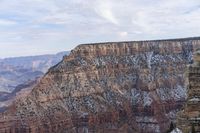 a large cliff surrounded by canyon covered in snow and rock formations is near the edge of a canyon