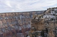 a large cliff surrounded by canyon covered in snow and rock formations is near the edge of a canyon