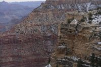 a large cliff surrounded by canyon covered in snow and rock formations is near the edge of a canyon