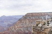 a large cliff surrounded by canyon covered in snow and rock formations is near the edge of a canyon