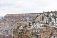 a large cliff surrounded by canyon covered in snow and rock formations is near the edge of a canyon