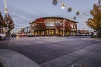 a large commercial building in a town setting on the corner of a street with a line of lights and people crossing the road