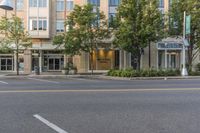 two streets and buildings with trees lined the curb and outside the building that is a large sign hanging above it