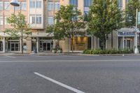 two streets and buildings with trees lined the curb and outside the building that is a large sign hanging above it