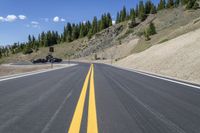 a view down an asphalt roadway at the bottom of a mountain near a house with a truck driving through it