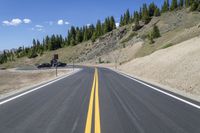 a view down an asphalt roadway at the bottom of a mountain near a house with a truck driving through it